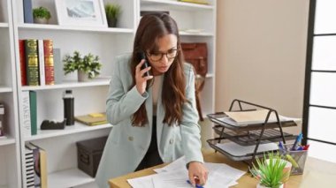 Genç, güzel İspanyol iş kadını. Belgeleri okuyor. Ofiste akıllı telefondan konuşuyor.