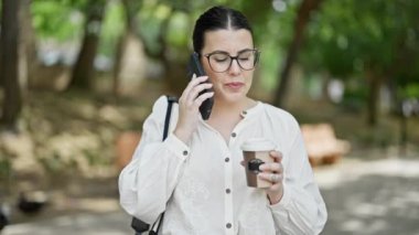 Genç ve güzel İspanyol kadın akıllı telefon kullanıyor. Parkta kahve içiyor.