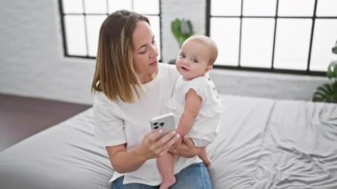 Sıcak yatak odasında, kendinden emin bir anne ve mutlu kızı birlikte biraz eğleniyorlar, yatakta oturmuş akıllı telefon ekranlarına bakıyorlar..