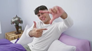 Genç İspanyol adamın neşeli yatak odası anı pijama giymiş elleri ve parmaklarıyla bir fotoğraf çerçevesi yapıyor.