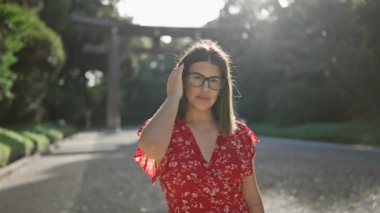 Neşeli, güzel, gözlüklü İspanyol kadın kendinden emin bir şekilde poz veriyor, Tokyo 'nun meiji türbesine gülümsüyor, mutluluğu şaşırtıcı gülüşünün içinden açıkça yayılıyor.