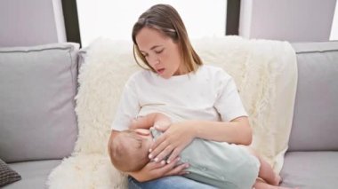 Evdeki rahat koltukta oturan yorgun anne bebeğini sevgiyle emziriyor, esniyor, anneliğin gerçekliğini gösteriyor.