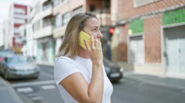Genç sarışın kadın caddede telefonla konuşuyor.