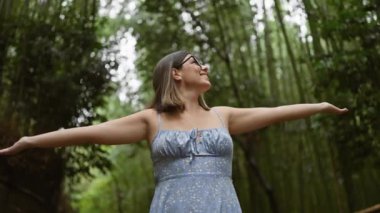 Neşeli İspanyol kadın Kyoto 'nun bambu ormanında özgürlüğü kucaklıyor, gülümsüyor, kollarını açmış etrafa bakıyor. Güzel, kendine güvenen, kaygısız gözlüklü Latin yetişkin Japonya 'nın yeşil güzelliğinin tadını çıkarıyor..