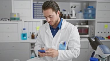 Young hispanic man scientist smiling confident using smartphone at laboratory