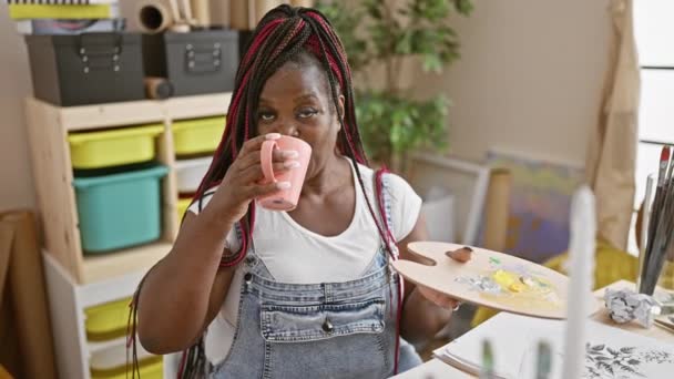 自信的非洲裔美国女艺术家在一间五颜六色的艺术工作室里一边微笑着一边喝咖啡 — 图库视频影像