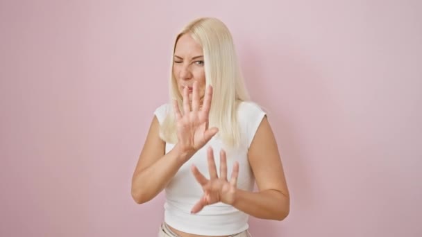 厌恶的金发女子表现出厌恶的反应 用双手在孤立的粉色背景上做着可怕的手势 — 图库视频影像