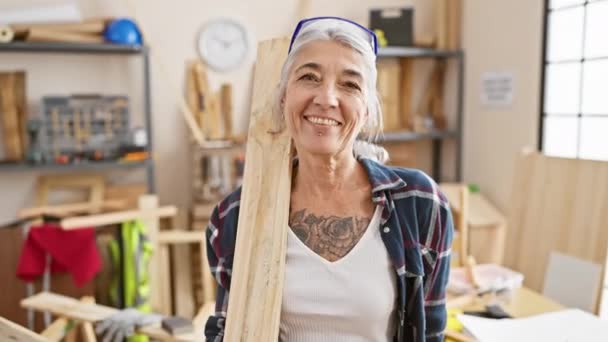 笑顔の灰色の髪のミドル年齢の女性大工は誇らしげに彼女の大工のワークショップで木製のペンキを保持しています — ストック動画