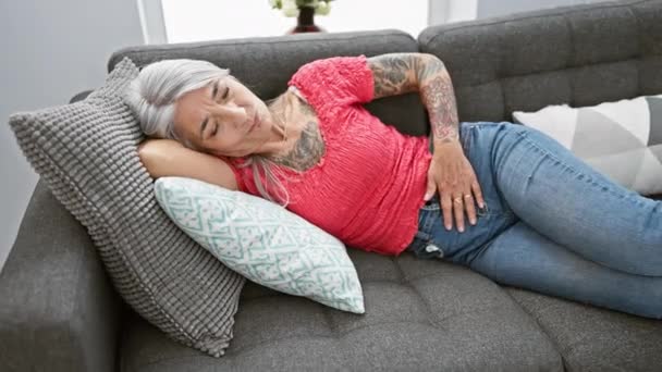 心配した中年の女性 優雅に灰色の髪をしていて 休んでいる間 不幸にも彼女のリビングルームのソファーに横たわっています — ストック動画
