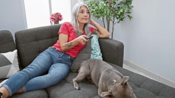 自信的中年妇女 对着宠物狗开心地笑着 在舒适的室内沙发上享受着轻松的电影时光 — 图库视频影像