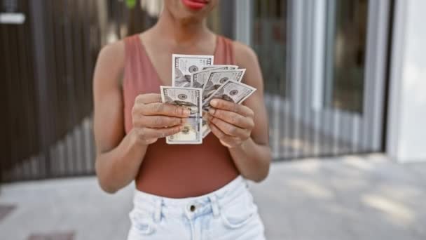 自信を持ってアフリカ系アメリカ人女性は喜んで日当たりの良い街の通りで美しい笑顔で彼女のドルを数えます — ストック動画