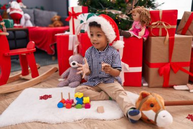 Afrikalı Amerikalı çocuk evde Noel hediyeleriyle yerde oturmuş oyuncaklarla oynuyor.
