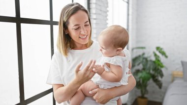 Kendine güveni tam bir anne oturma odasında duruyor, sevgiyle gülümseyen kızını kollarına alıyor, evde mutlu bir anı paylaşıyor.