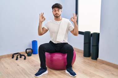 Sakallı İspanyol bir adam yoga odasında pilatese oturmuş rahatlıyor ve parmaklarıyla meditasyon hareketi yaparken gözleri kapalı gülümsüyor. yoga konsepti. 