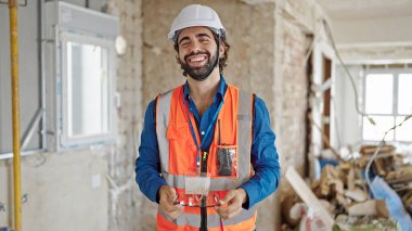 Genç İspanyol mimar inşaat alanında kendine güvenen gözlüklü gülümsüyor.