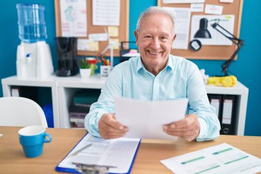 Orta yaşlı, kır saçlı bir iş adamı ofiste evrak okuyor.