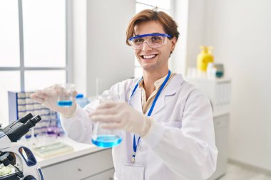 Young caucasian man scientist pouring liquid on test tube at laboratory