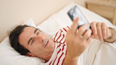 Yatakta uzanmış akıllı telefon kullanan orta yaşlı bir adam yatak odasına şaşırdı.