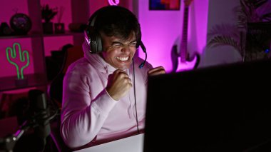 Çekici, İspanyol asıllı genç adam video oyunu zaferini karanlık oyun odasında büyük bir gülümsemeyle kutluyor.