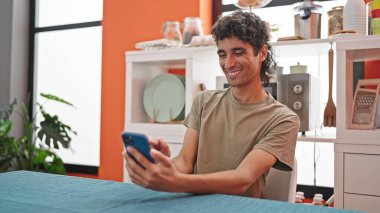 Genç İspanyol adam yemek masasında akıllı telefon kullanıyor.