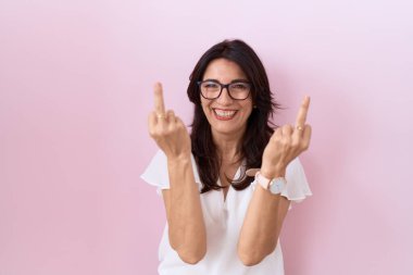 Middle age hispanic woman wearing casual white t shirt and glasses showing middle finger doing fuck you bad expression, provocation and rude attitude. screaming excited 