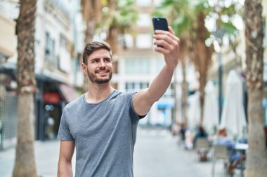 Kafkasyalı genç adam gülümsüyor. Sokakta akıllı telefonun yanında özçekim yapıyor.