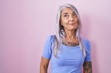 Pembe arka planda duran orta yaşlı bir kadın gülümsüyor ve yan tarafa bakıyor.. 