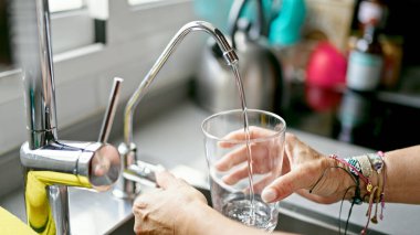 Orta yaşlı İspanyol kadın mutfakta bardağa musluk suyu döküyor.