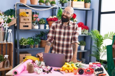 Young bald man florist smiling confident using laptop at flower shop