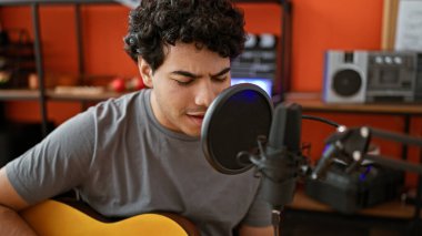 Young latin man musician singing song playing classical guitar at music studio