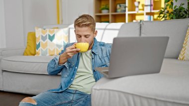 Young caucasian man using laptop drinking coffee at home