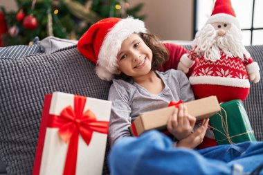 Sevimli Çinli kız elinde hediyeyle evdeki Noel ağacının yanındaki koltukta oturuyor.