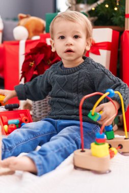 Sevimli sarışın çocuk evde Noel hediyeleriyle yerde oyuncaklarla oynuyor.