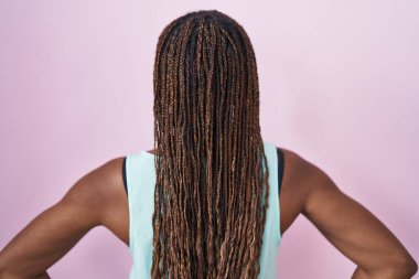 Pembe arka planda duran Afrikalı Amerikalı kadın geriye doğru bakıyor kolları vücudunda. 