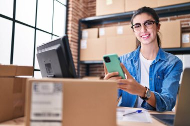Genç, güzel, İspanyol bir kadın. İş kadını. Ofiste dizüstü bilgisayar ve akıllı telefon kullanıyor.
