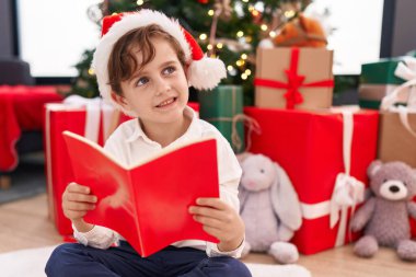 Sevimli İspanyol çocuk kitap okuyor. Evdeki Noel ağacının yanında oturuyor.