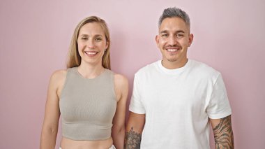 Kadın ve erkek bir arada durmuş pembe arka planda gülümsüyor.