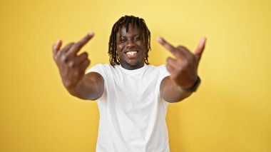 Afro-Amerikalı adam gülümsüyor. İzole edilmiş sarı arka planda orta parmak hareketi yapıyor.