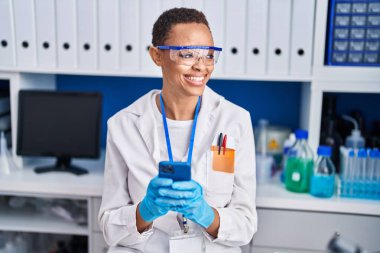 Laboratuvarda akıllı telefon kullanarak gülümseyen Afrikalı Amerikalı bilim kadını.