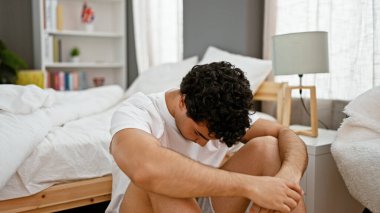 Genç Latin adam yatak odasında yerde otururken stresli.