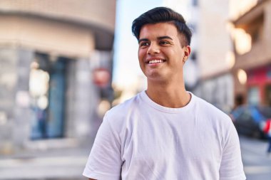 Young hispanic man smiling confident looking to the side at street