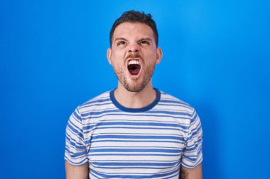 Mavi arka planda öfkeli ve kızgın bağıran öfkeli ve öfkeli genç bir İspanyol. Öfkeyle bağırıyor. öfke ve agresif konsept. 