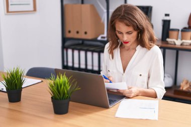 Young beautiful hispanic woman business worker using laptop reading document at office
