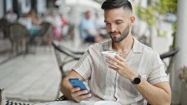 Genç İspanyol adam akıllı telefon kullanıyor. Kahve dükkanının terasında kahve içiyor.