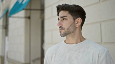 Latin kökenli genç adam ciddi bir ifadeyle sokağa bakıyor.