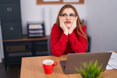 Young redhead woman business worker tired sitting on table at office