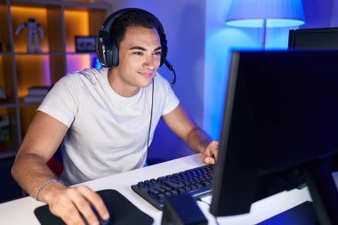 Oyun odasında bilgisayar kullanarak video oyunu oynayan İspanyol asıllı genç adam.