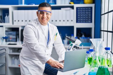 Laboratuvarda dizüstü bilgisayarını kullanarak gülümseyen genç Latin bilim adamı.