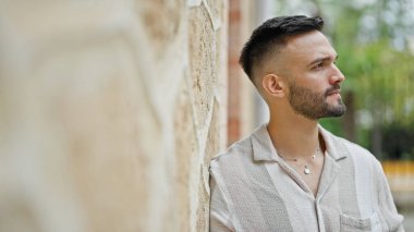 Sokakta duvara yaslanmış ciddi bir ifadeyle yan tarafa bakan İspanyol genç adam.