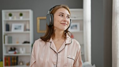 Genç bir kadın yatak odasında müzik dinliyor.